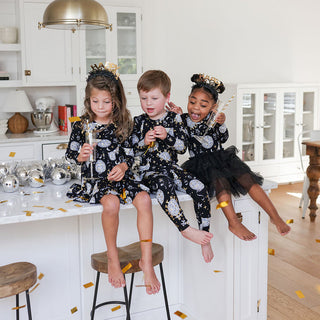 Posh Peanut Ruffle Twirl Dress - Midnight Bash
Three children in matching black and white outfits sitting on a kitchen counter.