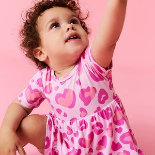 Posh Peanut Ruffled Twirl Bodysuit Dress - Love Leopard
Child wearing a pink dress with heart patterns against a pink background