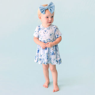 Posh Peanut Ruffled Twirl Bodysuit Dress - Trista
Baby wearing a floral dress with a blue bow on a light blue background