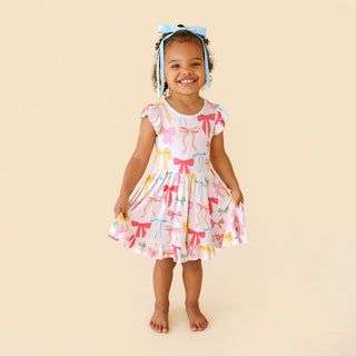 Posh Peanut Ruffled Twirl Dress - Shawna
Young girl wearing a dress with bow pattern on a beige background
