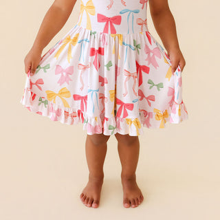 Posh Peanut Ruffled Twirl Dress - Shawna
Child wearing a dress with colorful bow pattern on a beige background