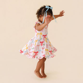 Posh Peanut Ruffled Twirl Dress - Shawna
Child wearing a colorful dress with bow patterns on a beige background