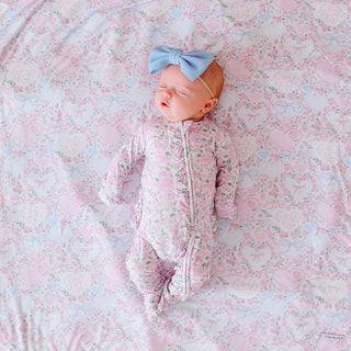 Posh Peanut Ruffled Zippered Footie - Annabeth
Newborn baby in a floral onesie and bow headband lying on a floral blanket