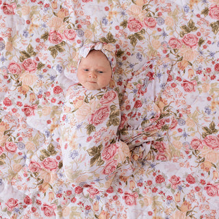 Posh Peanut Swaddle Headband Set - Kristiana
A baby swaddled in a matching floral muslin blanket with a coordinating headband, lying on a quilted floral blanket. The fabric features a vintage rose pattern in soft pink, peach, red, and green on a white background.