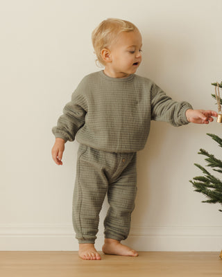 Quincy Mae Textured Sweat Set - Forest
Child wearing a green outfit standing next to a small Christmas tree indoors.