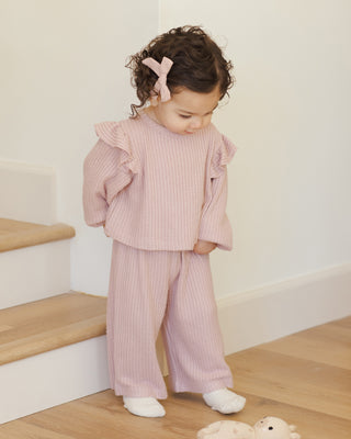 Quincy Mae Ruffle Cozy Set - Rose Child wearing a pink ribbed outfit standing on a wooden floor with a white wall background