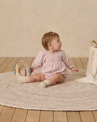 Quincy Mae Eden Romper - Bows
Baby in a pink dress sitting on a textured rug with a wooden floor and beige wall in the background