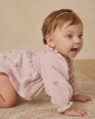 Quincy Mae Eden Romper - Bows
Baby in a pink outfit with bow patterns on a beige background