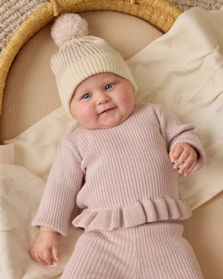 Quincy Mae Beanie - Lilac
Baby in pink ribbed outfit and cream hat with pom-pom, lying on a textured blanket.