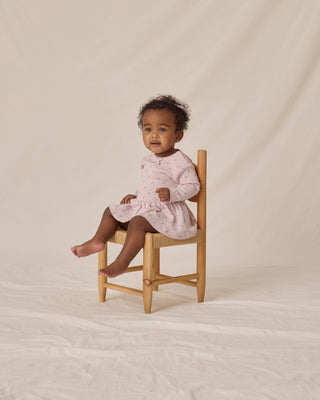 Quincy Mae Pointelle Skirted Bodysuit - Lilac
Baby in a pink dress sitting on a wooden stool against a beige background