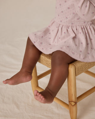 Quincy Mae Pointelle Skirted Bodysuit - Lilac
Child wearing a pink dress with a subtle pattern, sitting on a wicker chair.