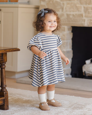 Quincy Mae Darla Dress - Ocean Stripe
Child wearing a striped dress standing in a room with a fireplace.