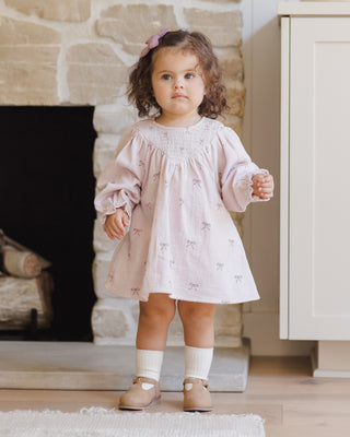 Quincy Mae V Smocked Dress - Bows
Young girl in a pink dress standing in a room with a stone fireplace.