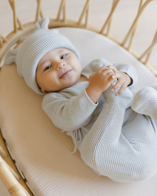 Quincy Mae Baby Bear Beanie - Ice Blue
Baby in a light blue outfit and hat lying on a beige cushion.