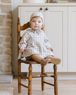Quincy Mae Simone Dress - Blue Plaid
Baby in a checkered outfit sitting on a wooden chair indoors.
