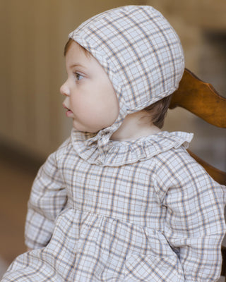 Quincy Mae Simone Dress - Blue Plaid
Child wearing a checkered bonnet and dress sitting on a wooden chair.