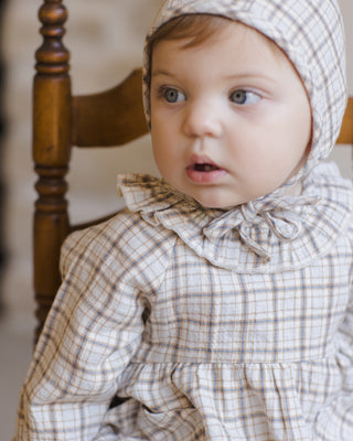 Quincy Mae Simone Dress - Blue Plaid
Baby wearing a checkered dress and bonnet sitting on a wooden chair.
