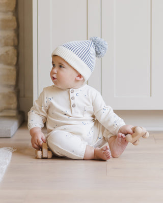 Quincy Mae Henley Bubble Jumpsuit - Moons
Baby sitting on a wooden floor wearing a white outfit and striped hat.