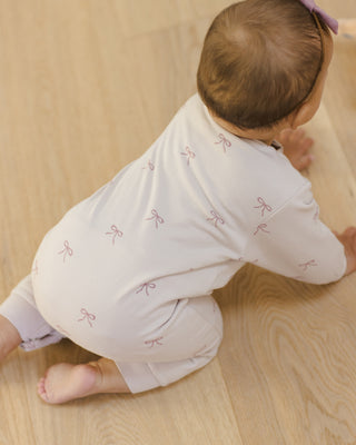 Quincy Mae Relaxed Fleece Jumpsuit - Bows
Baby in light-colored outfit with bow patterns on a wooden floor