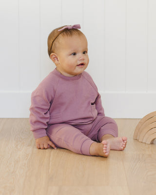 Quincy Mae Pocket Sweatshirt & Sweatpant Set - Mulberry
Baby in a pink outfit sitting on a wooden floor with a white wall background