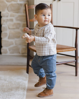 Quincy Mae Zion Shirt - Blue Plaid
Child standing indoors holding a toy, wearing a checkered shirt and blue pants.