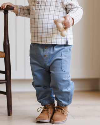 Quincy Mae Zion Shirt - Blue Plaid
Child wearing a plaid shirt, blue pants, and brown shoes standing next to a wooden chair.