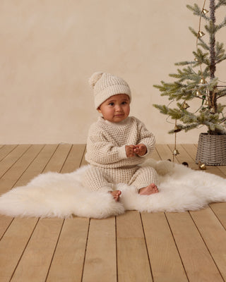 Quincy Mae Beanie - Natural
Baby in a knitted outfit sitting on a white rug next to a small Christmas tree.