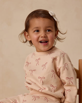 Quincy Mae Relaxed Fleece Sweatshirt & Sweatpant Set - Red Bows
Child wearing a pink sweater with bow patterns on a beige background