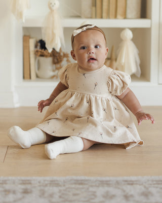 Quincy Mae Darla Dress - Magic
Baby in a beige dress sitting on a wooden floor with a neutral background