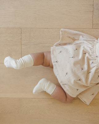 Quincy Mae Darla Dress - Magic
Baby in a white outfit with black patterns on a wooden floor