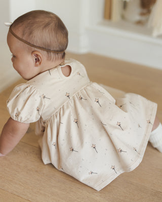 Quincy Mae Darla Dress - Magic
Baby in a cream dress with floral pattern on a wooden floor