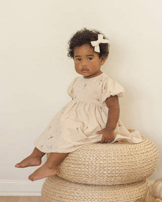 Quincy Mae Darla Dress - Magic
Child in a light dress sitting on a woven stool against a plain background