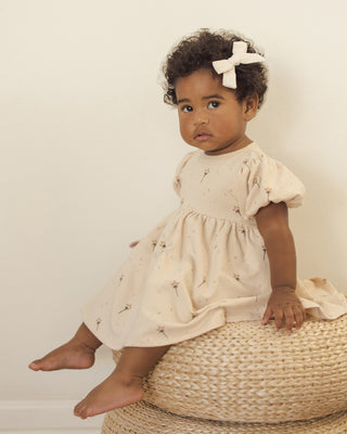 Quincy Mae Darla Dress - Magic
Young child in a light dress sitting on a woven stool against a plain background