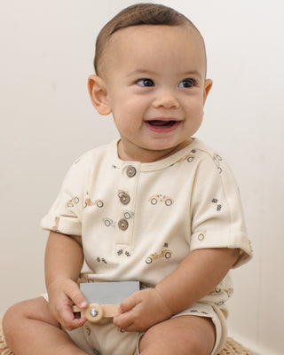Quincy Mae Short Sleeve One Piece - Race Car
Baby wearing a cream-colored outfit with button details, sitting on a light surface.