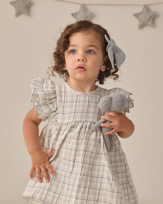 Quincy Mae Alina Dress - Blue Plaid
Child wearing a plaid dress holding a toy with star decorations on the wall.