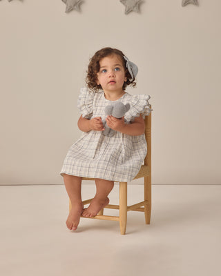 Quincy Mae Alina Dress - Blue Plaid
Child in a checkered dress holding gray toy hearts, sitting on a wooden stool against a neutral background.