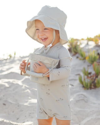 Quincy Mae Bucket Hat - Sage
Child in a light-colored outfit and hat standing on a sandy beach.