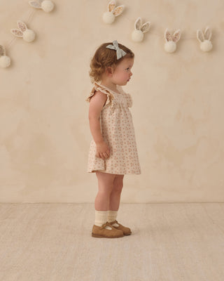 Quincy Mae Flutter Dress - Strawberries
Young girl in a floral dress standing against a beige wall with decorative bunny elements.