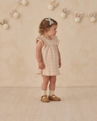 Quincy Mae Flutter Dress - Strawberries
Young girl in a floral dress standing against a beige wall with decorative elements.