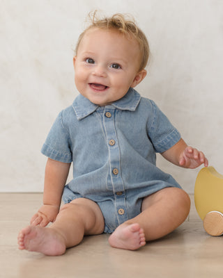 Quincy Mae Matteo Romper - Chambray
Baby wearing a denim romper sitting on a wooden floor with a white wall background