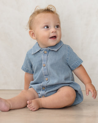 Quincy Mae Matteo Romper - Chambray
Baby wearing a denim romper sitting on a wooden floor with a white wall background