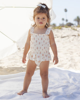 Quincy Mae Smocked One Piece Swimsuit - Garden Rose
Young child in a floral swimsuit standing on a sandy beach.