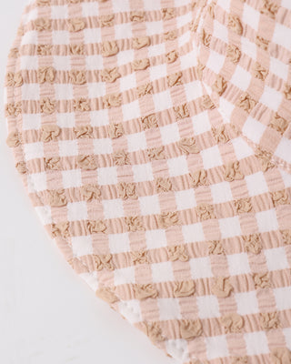 Quincy Mae Sun Hat - Melon Check
Close-up of a beige and white checkered fabric with ruffled edges on a light gray background