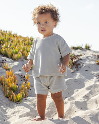 Quincy Mae Terry Top + Short Set - Sage
Child in light gray outfit standing on a sandy beach with greenery.
