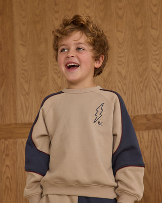 Play by Rylee & Cru Paneled Sweatshirt - Stone Child wearing a beige and navy sweatshirt with a logo against a wooden background