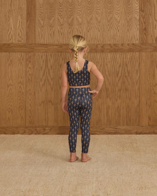 Play by Rylee & Cru Swift Sports Bra - Vintage Bloom Play by Rylee & Cru Basic Legging - Vintage Bloom Child wearing a navy patterned outfit standing against a wooden paneled wall.