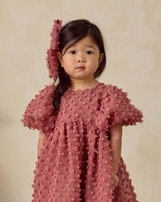 Noralee Everly Bow - Raspberry
Young girl wearing a pink textured dress and matching headband against a beige background