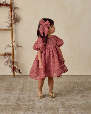 Noralee Everly Bow - Raspberry
Young girl in a pink dress standing in a room with a wooden ladder and decorative plants.