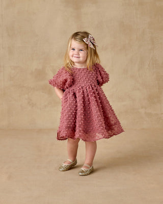 Noralee Luna Dress - Raspberry
Young girl in a pink dress with a floral headband against a beige background