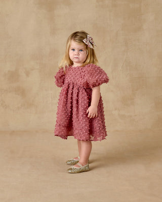 Noralee Luna Dress - Raspberry
Young girl wearing a pink dress with ruffled sleeves against a beige background